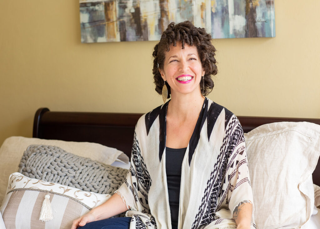 joyful woman sitting on bed, looking out towards white might be a window lighting her face