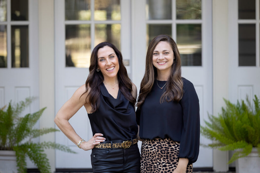 realtor team of two women standing front of white double doors of large house